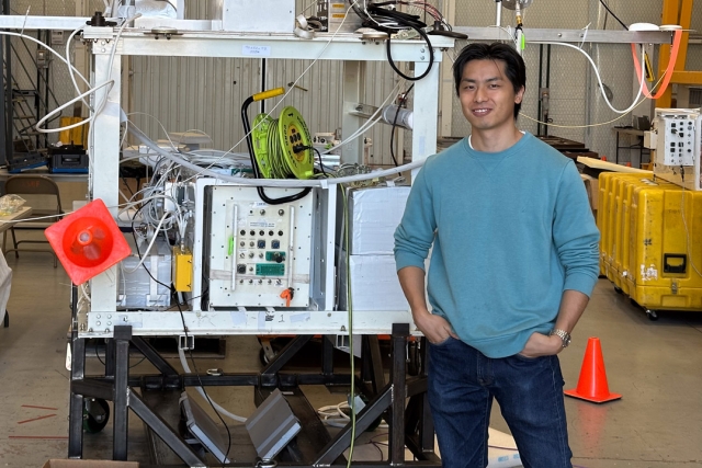 student Kazuma Noda stands with the BOOP! gondola in a warehouse setting.