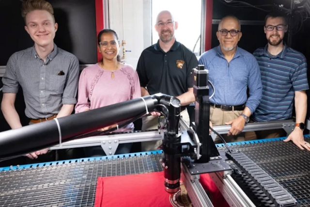 a group of students stands smiling in front of a textile machine.