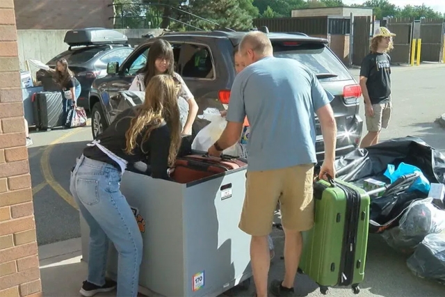 two students and an adult load a bin with items on move in day