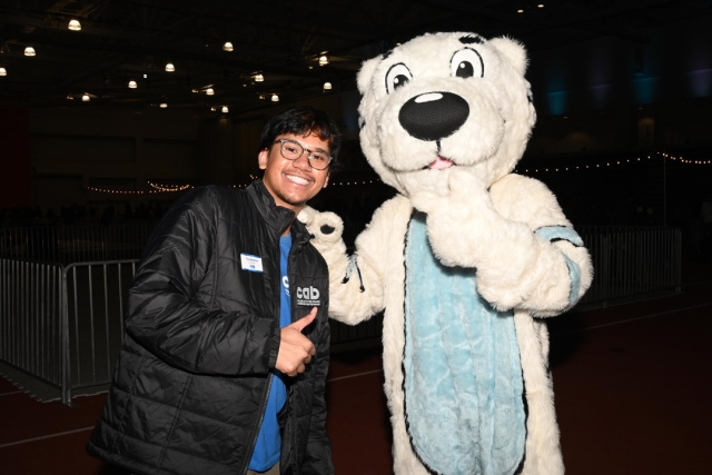 a young man in a black jacket stands with Roarie the white tiger who is the R I T freeze fest mascot.