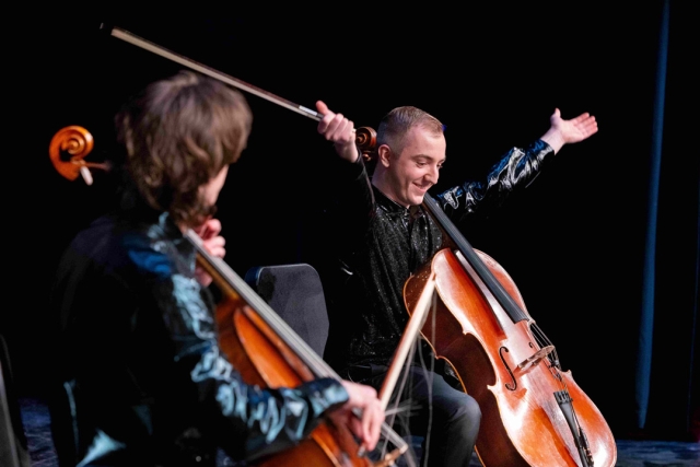 Two young men sit on stage with cellos.