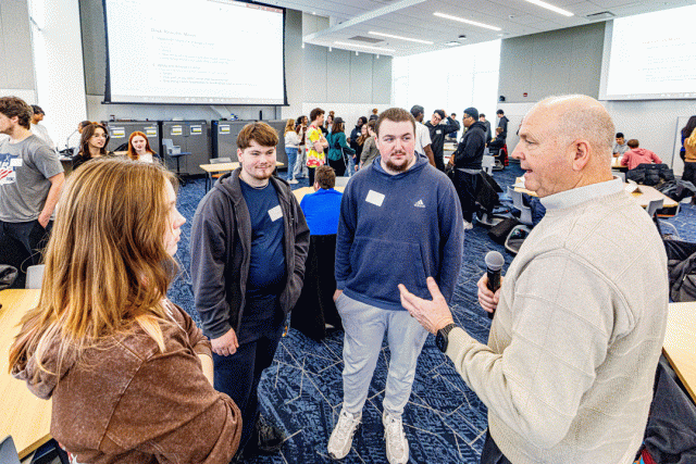 A group of four people stand speaking in a business classroom.