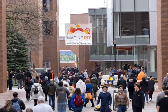 a crowd of people walk under a sign for Imagine R I T