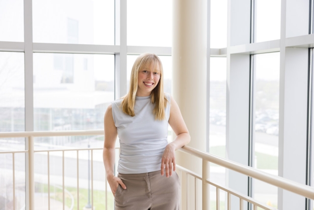 a woman with blonde hair stands in a brightly lit light atrium wearing neutral colored clothes