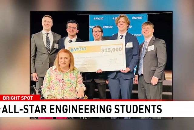 a group of students stand with a large check made out in the amount of fifteen thousand dollars from N Y S I D