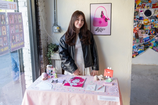 A student stands in front of a table displayed with pink art objects