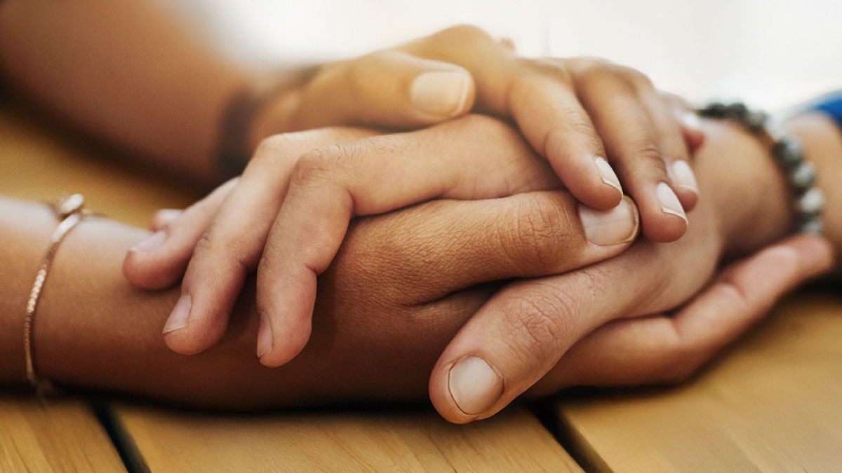 Closeup of two people holding hands in support.