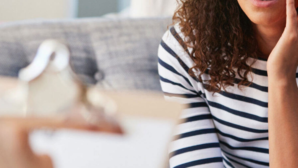 A person sitting in a chair with a clipboard, talking to another person sitting on a couch.