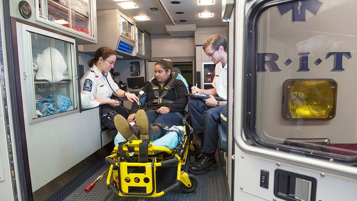 A person on a gurney in the back of an ambulance with two health professionals.