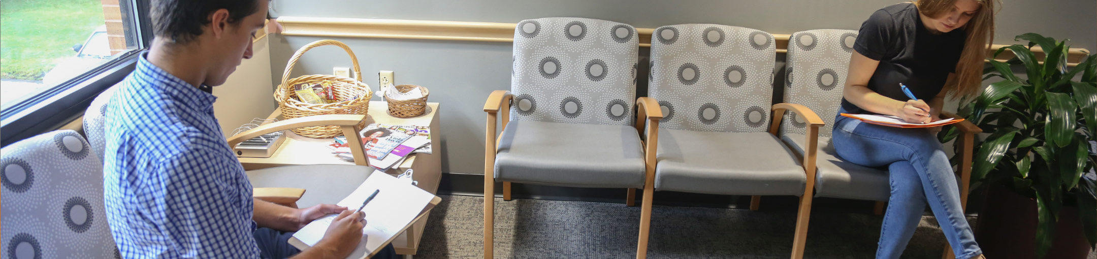 Two people sitting in a waiting room filling out forms.