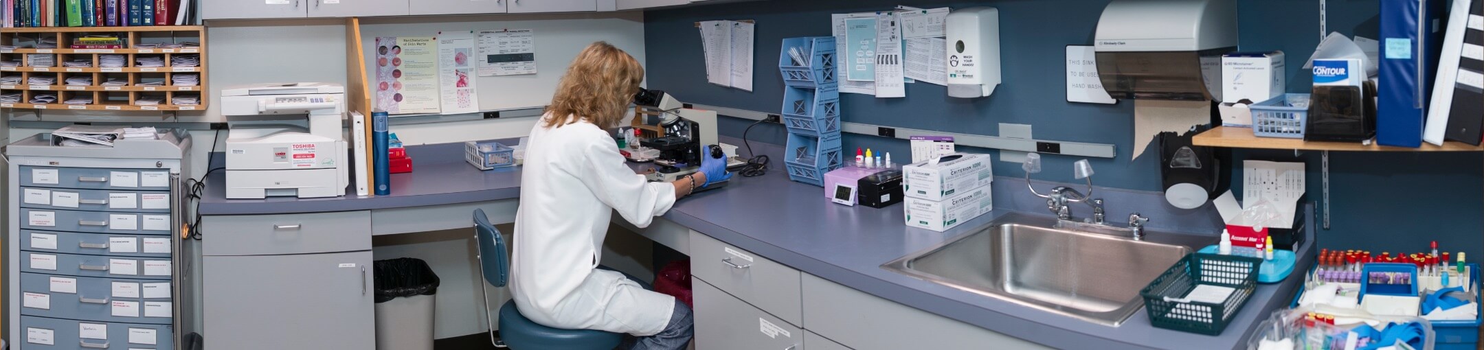 A lab technician looking at samples through a microscope in a lab.