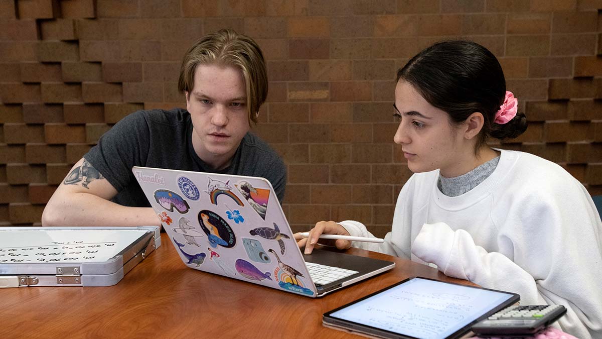 Two students sitting at a table looking at a laptop screen