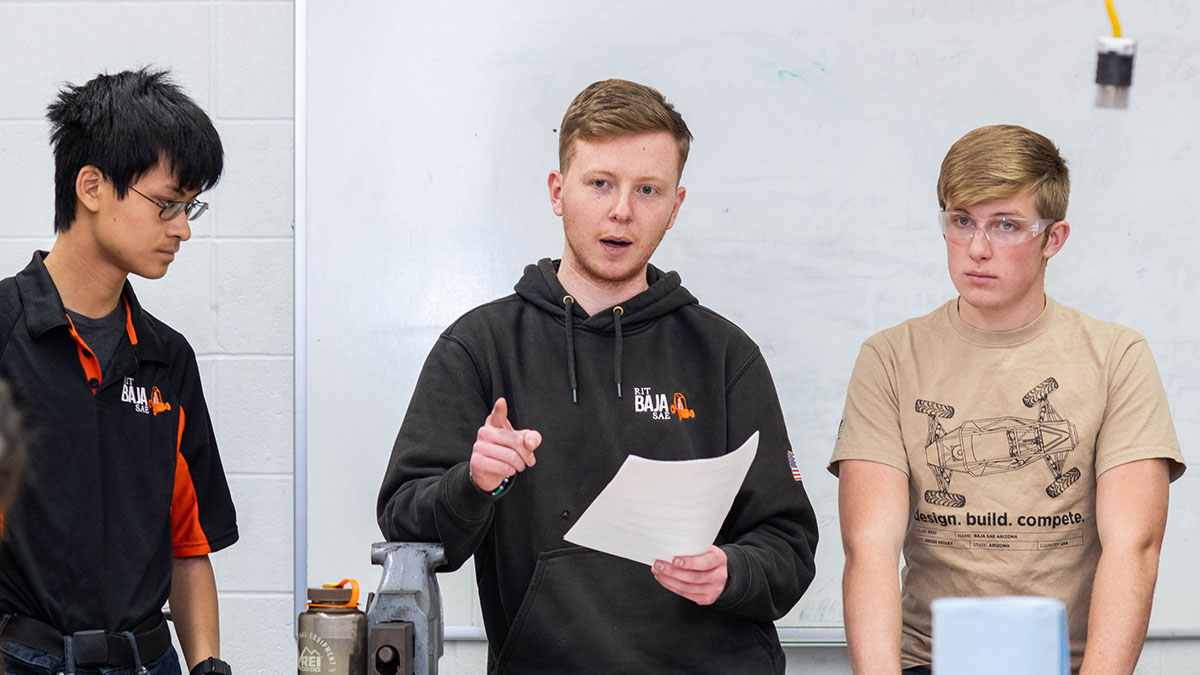 three students standing in a classroom giving a presentation.