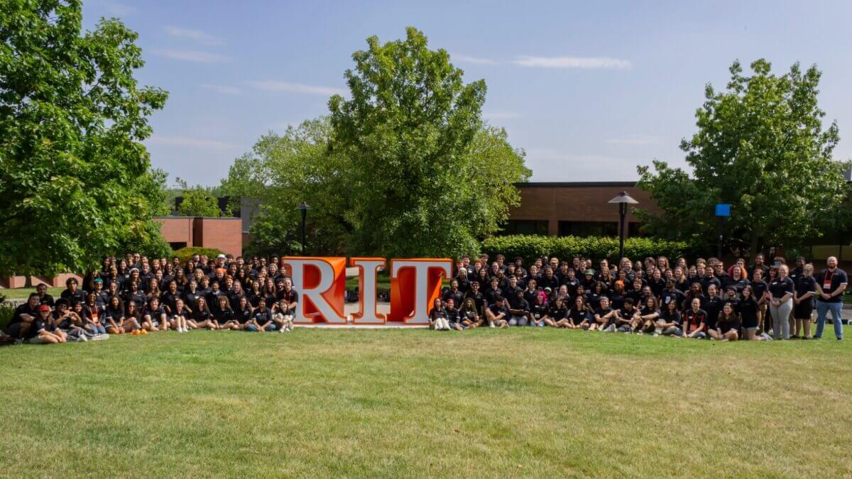 A group of Resident Advisors posing next to an RIT sign near Fountain Park on campus