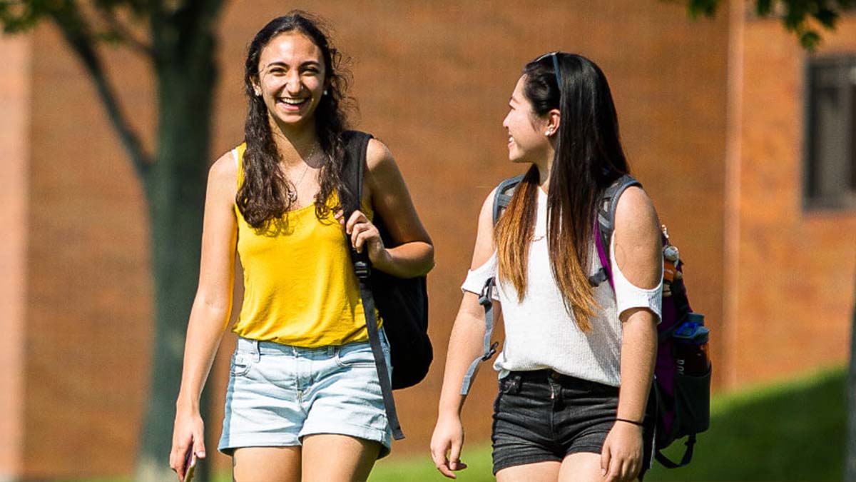 Two R I T students walking outside of a residence hall. 