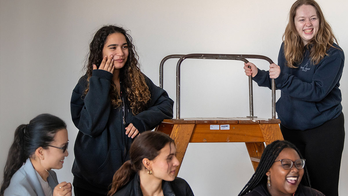 five students smiling and laughing, with one students standing on a ladder.