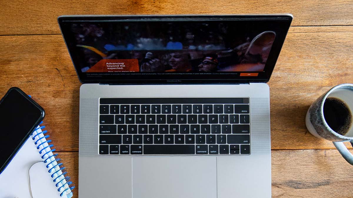 Overhead shot shows a laptop, coffee mug, and notebook on top of a wooden table