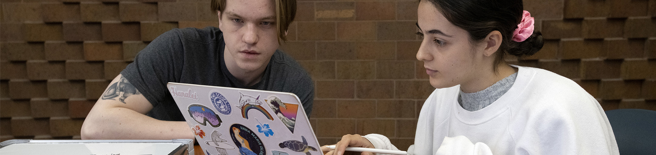 Two students sitting at a table looking at a laptop screen