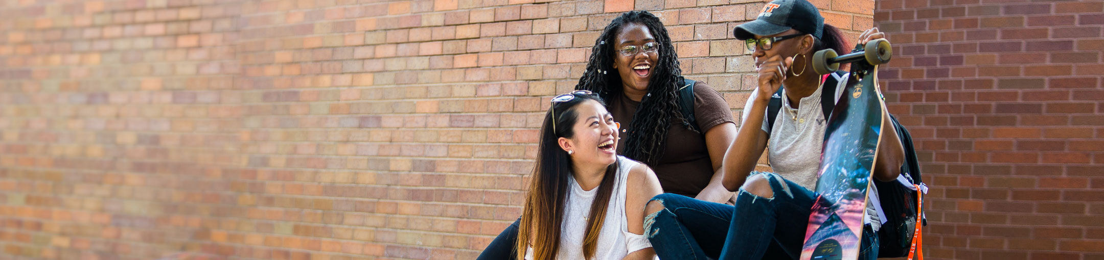 Three RIT students, laughing, outside in front of a brick wall.