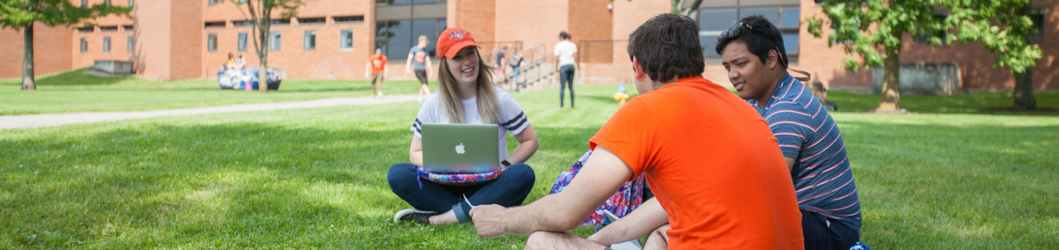 Three R I T students sitting in the lawn outside of a residence hall.
