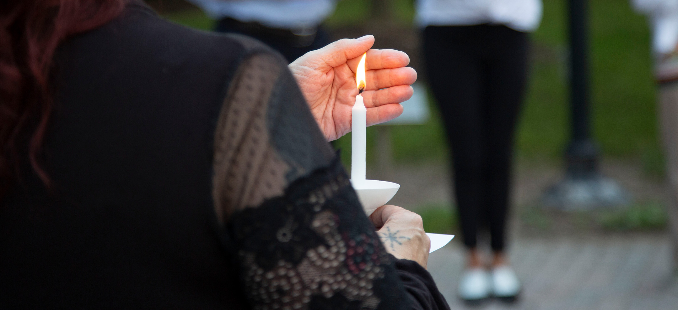Individual in a black shirt is shown holding a candle at a candlelight vigil