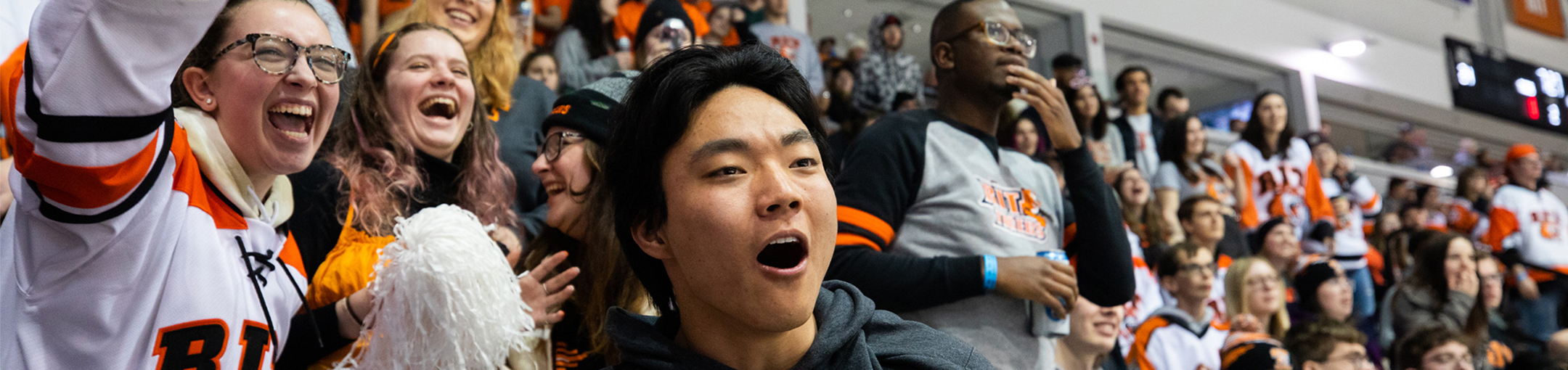 Students wearing R-I-T gear while cheering in the spectator section of a hockey game