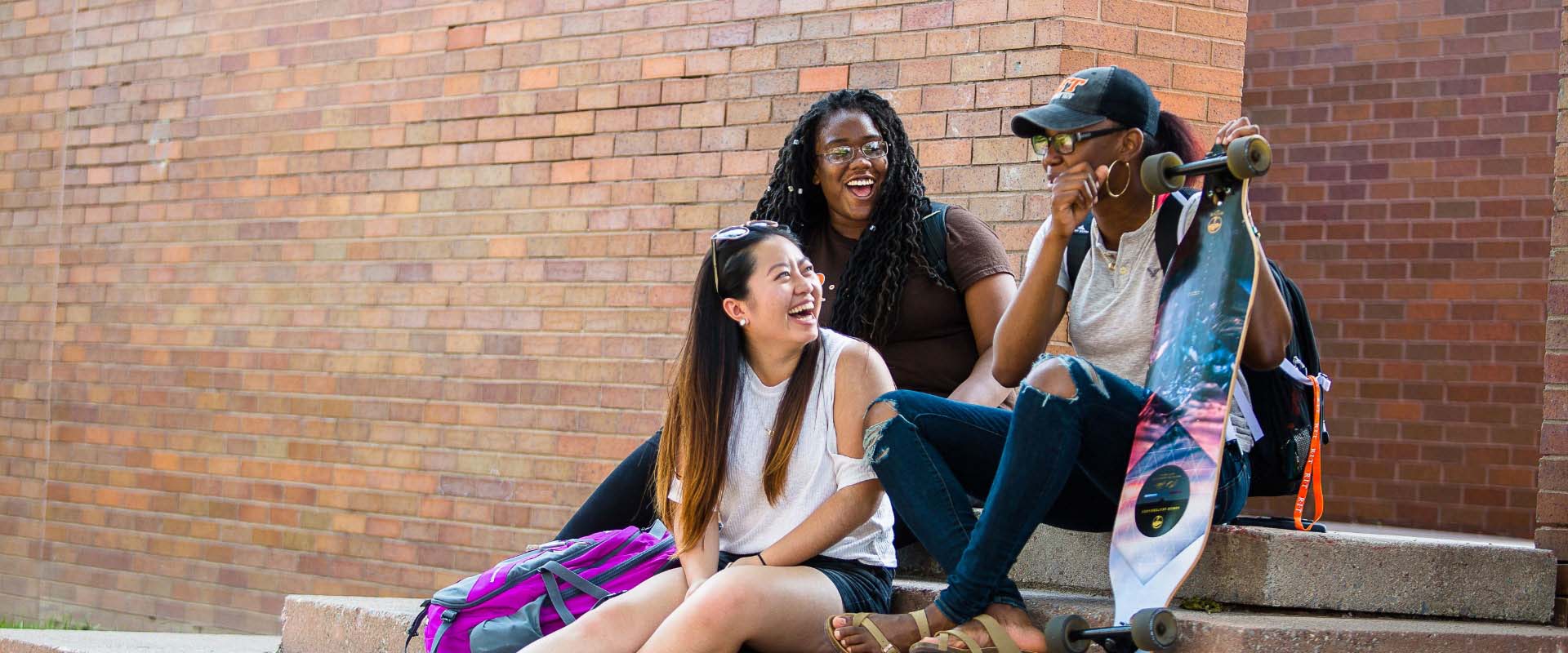 Three female students laughing while sitting on steps outdoors.