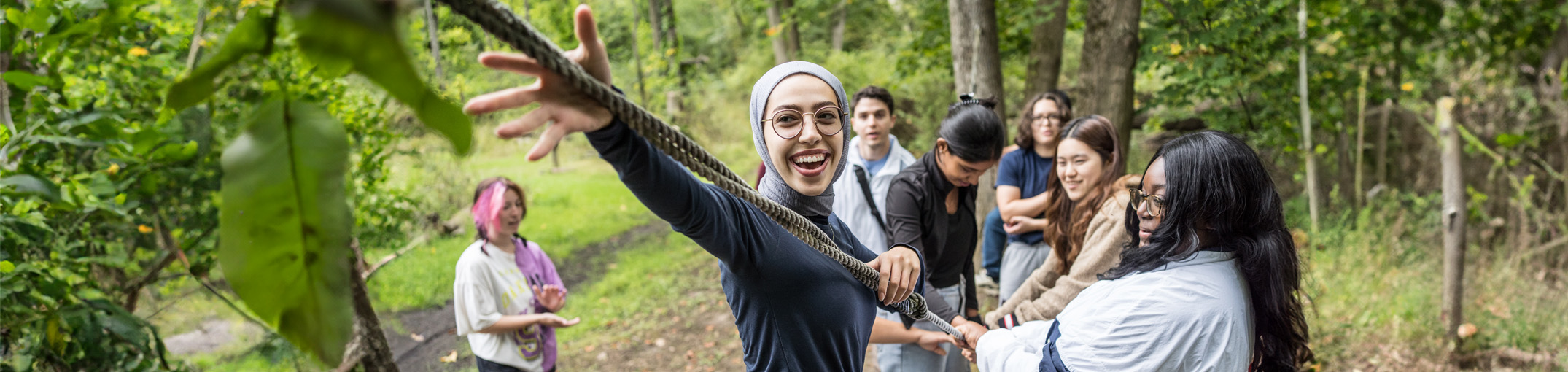 A student reaches out to grab a rope while other students hold onto the rope in the background