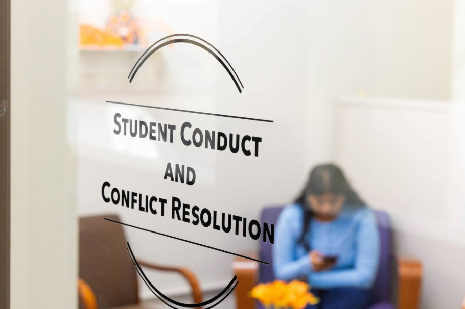 A student sitting in a waiting room at the student conduct and conflict resolution office at RIT looking at their phone