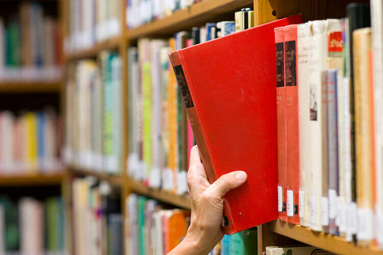 A hand grabbing a book off of a shelf in a library