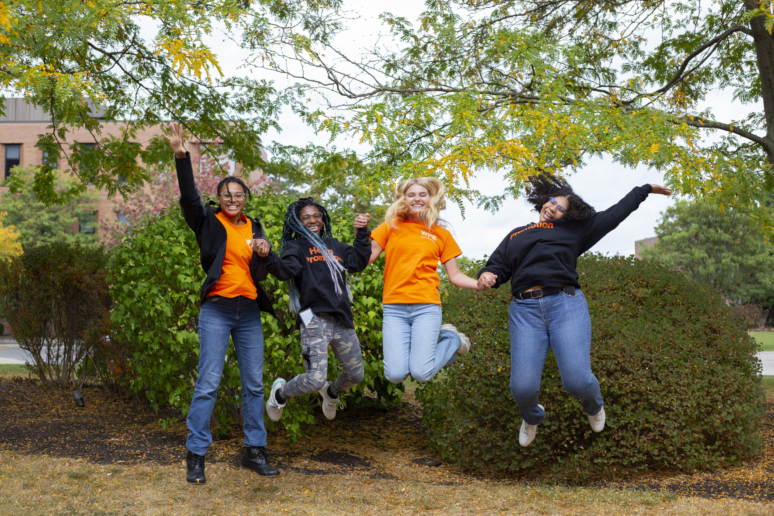 Four students jumping up in the air holding hands outside
