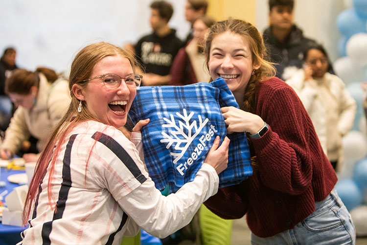 Two students smile and pose holding a FreezeFest blanket