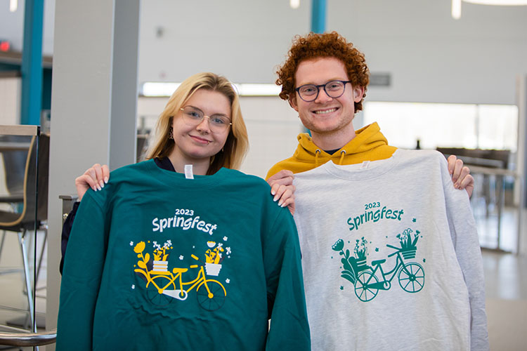 Two students hold up green and white SpringFest sweatshirts