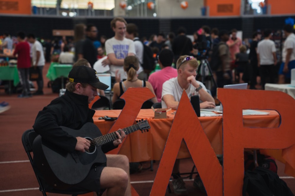 A student plays a black guitar in front of the stand for a fraternity at the Tigers Activities Fair.