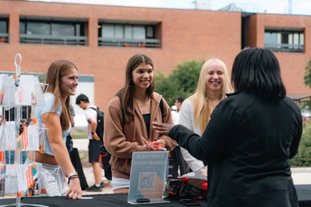 Students talk with a campus representative at a table display during a TigerFest event, with brochures and giveaway items visible.