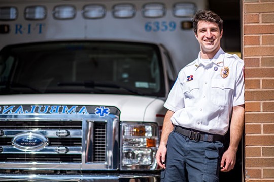 Oren Cohn poses for a photo in his RIT Ambulance uniform in front of one of the ambulance vehicles.