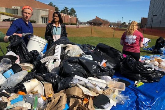 Students stand near pile of garabe outside.