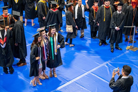Students in graduation caps and gowns pose for photo.