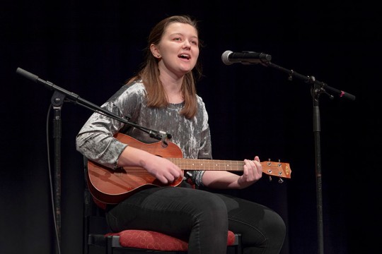 student playing guitar and singing into microphone.