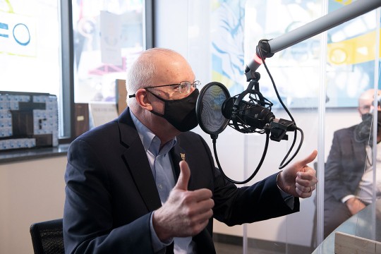 RIT President Munson wearing a mask and speaking into a microphone in a radio station.