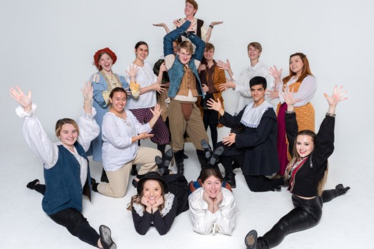 cast of a play posing with their hands in the air.