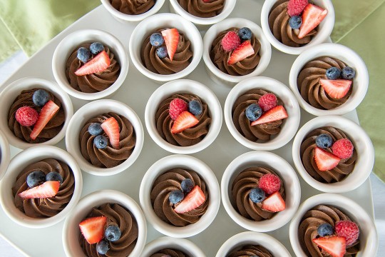 ramekins of chocolate pudding topped with blue berries, strawberry slice and a raspberry.