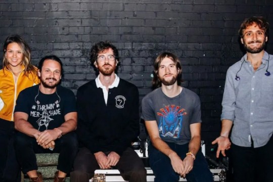 5 members of the band Mt Joy appear sitting in front of a black brick wall