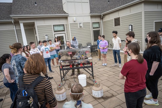 Tom Connelly speaks to students about maple sugaring as they gather around him in a circle