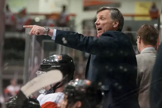 a man in a suit stands with a hockey team and points at the ice.