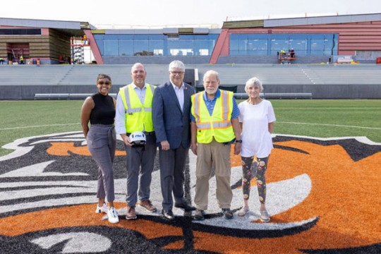 Five people standing on a sports field with a construction site in the background.