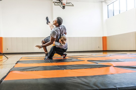 two students wrestle on an orange and black mat in a gymnasium