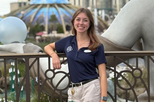 a college age woman in khaki pants and a blue polo shirt leans against a metal railing at Universal Studios Orlando