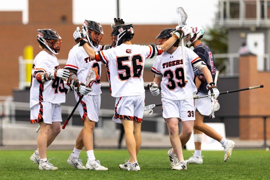 five R I T lacrosse players high five on a playing field in full gear