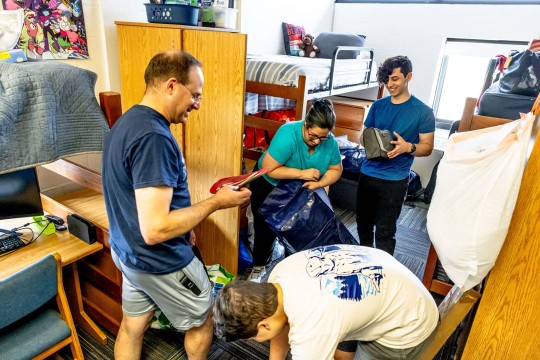 parents help their child move in to a dorm room.